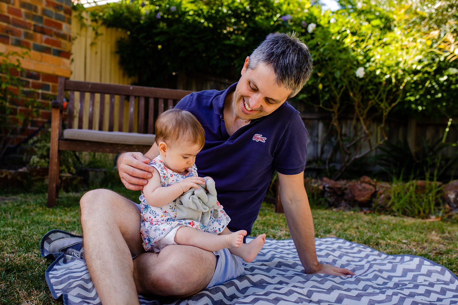 father sits on picnic rug holding his baby