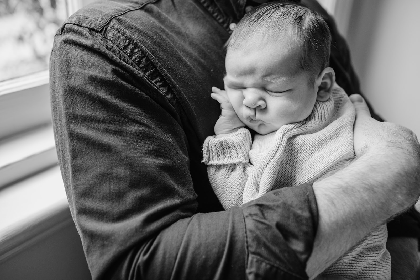 newborn cuddles into dad, black and white baby asleep
