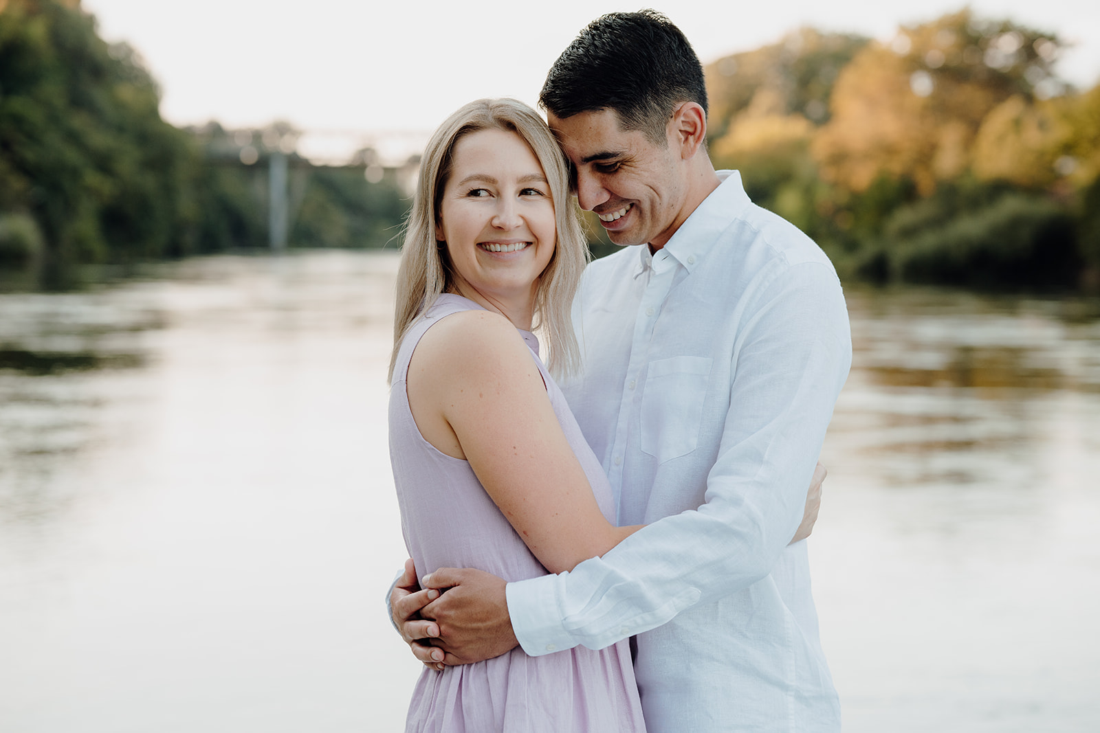 A couple standing in front of the waikato river with their photographer haley adele photography taking portraits of them