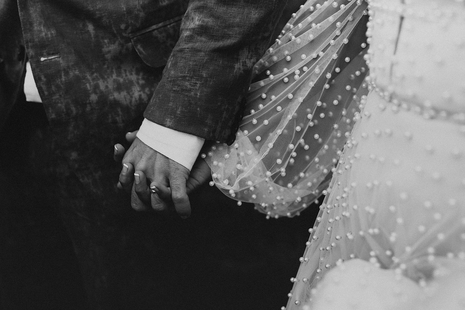 A black and white detail photograph of the couple holding hands.