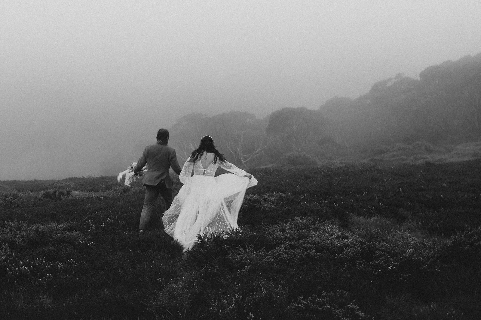 A black and white image of the bride and groom running through the hills on their elopement day.