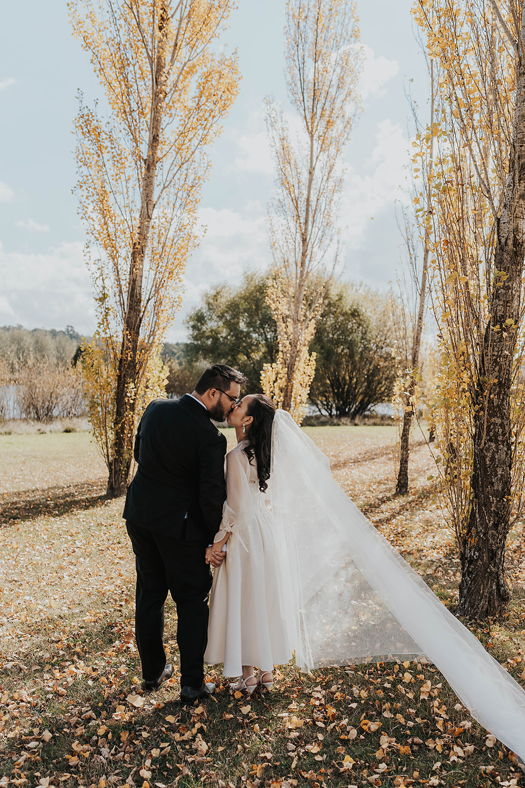 The married couple shares a kiss underneath the golden autumn trees in Daylesford.