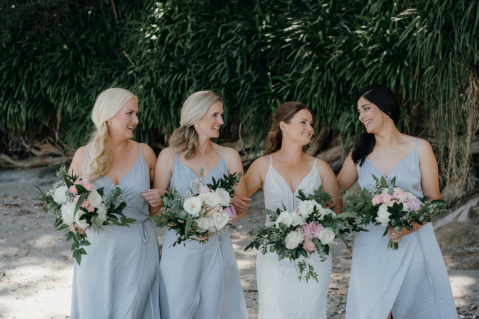 bridesmaids in BLAK dresses in a blue shade look at the bride. they are all holding green and white bouquets 