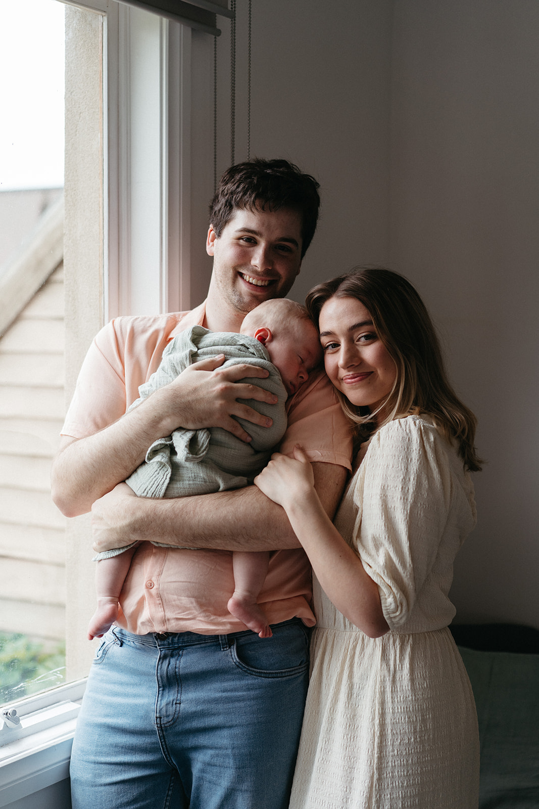 a couple smiling at the camera holding their three month old baby