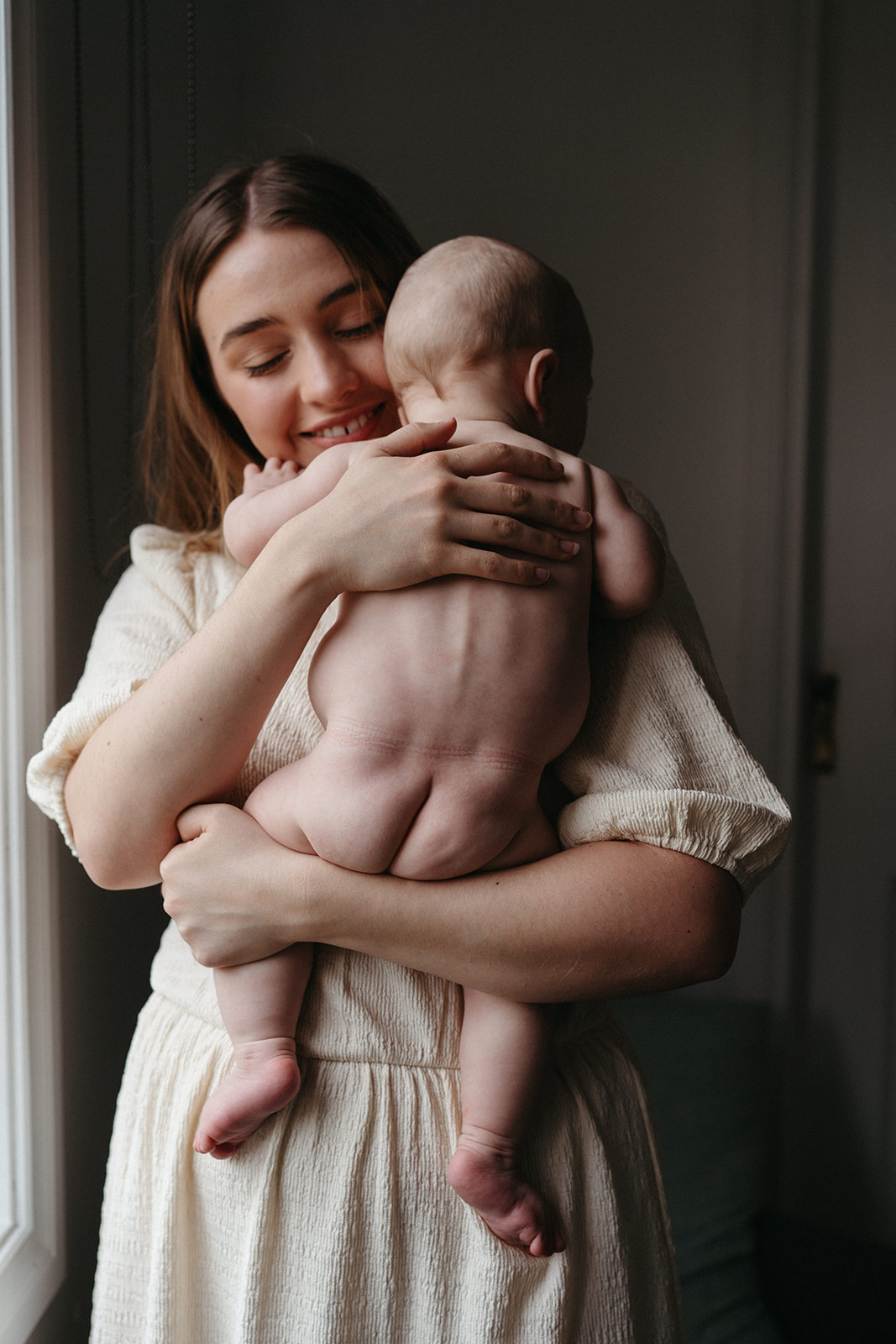 a mother holds her nude baby close to her chest and smiles