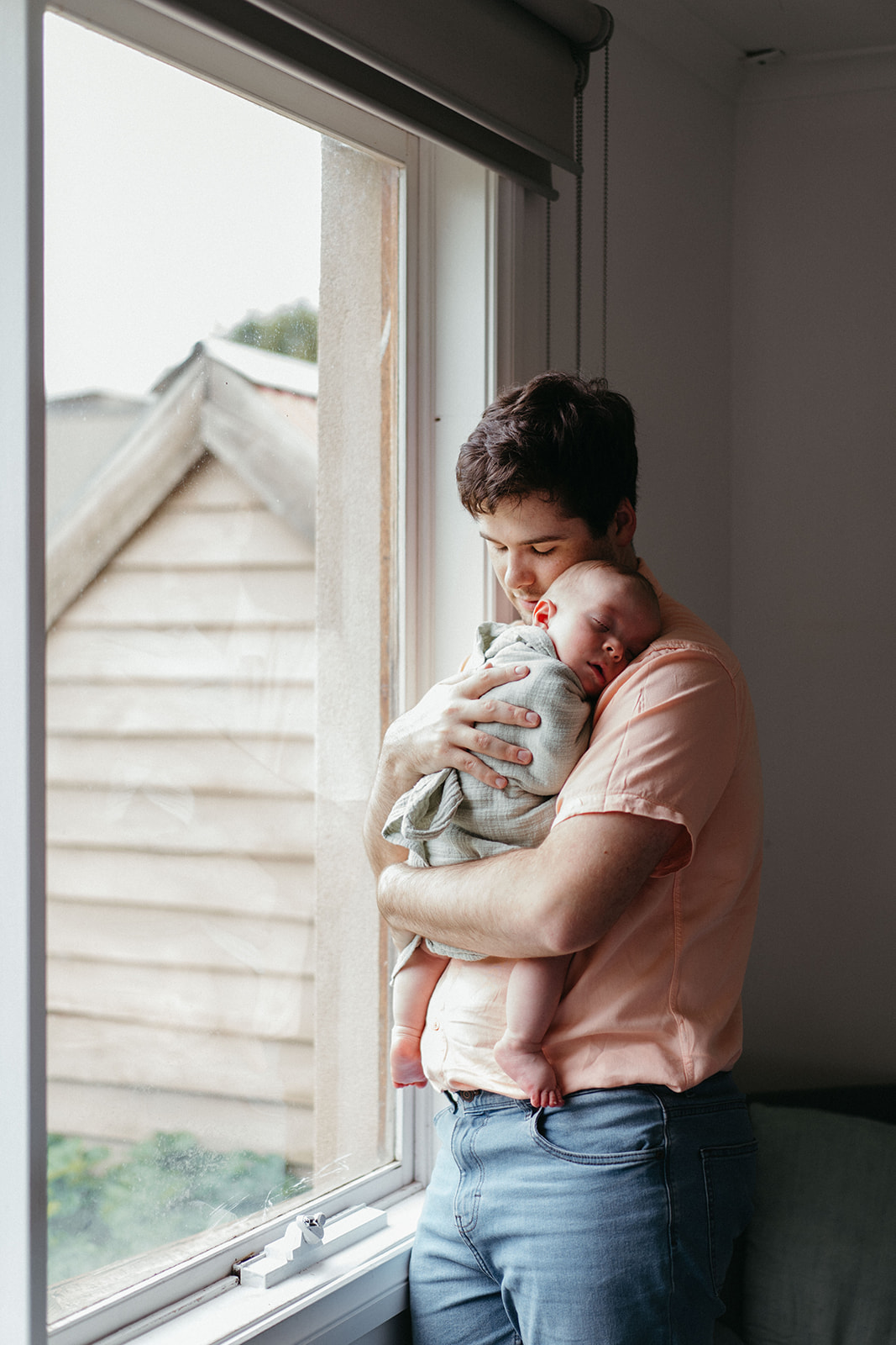 a photograph of a father holding his baby near a window