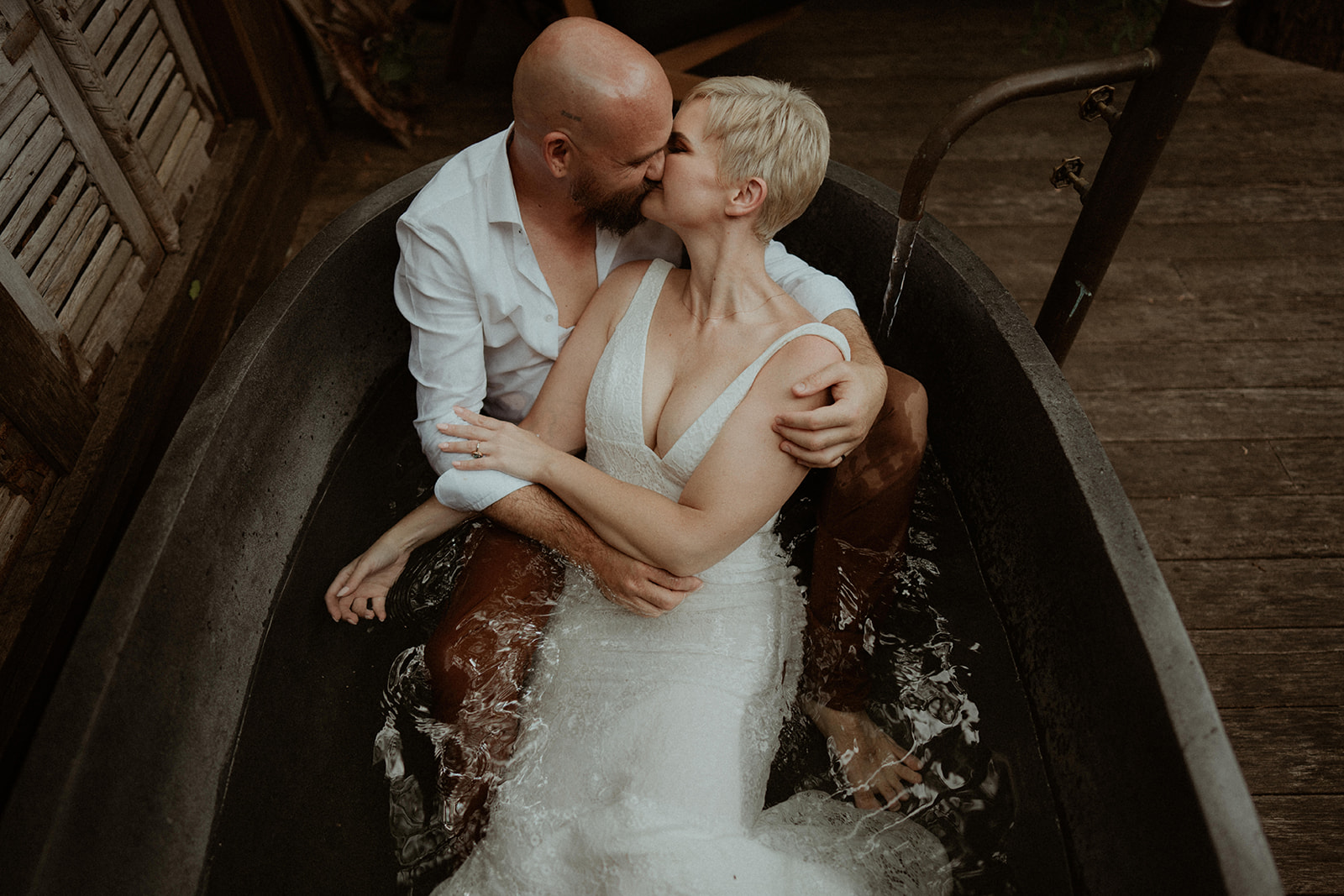 A bride and groom in a bath tub on an outdoor deck in Kangaroo Valley. The bathtub is filling up with water.