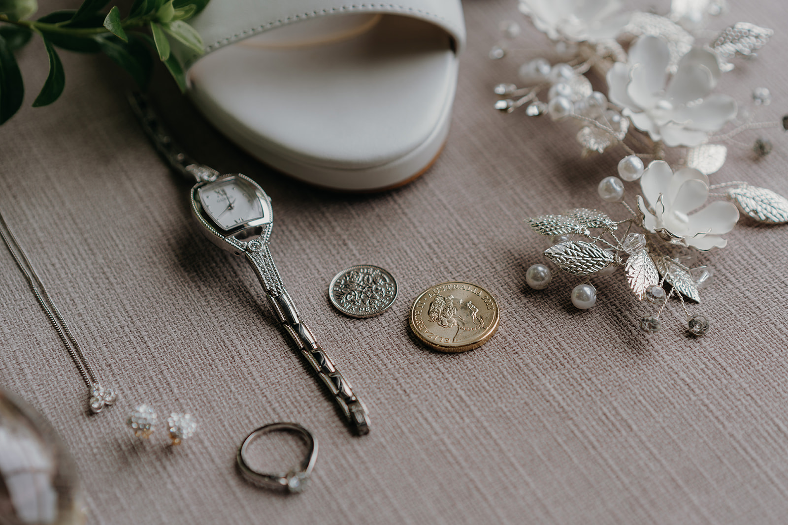 the brides rings and other jewellery are laid out of a cream cushion to be photographed 