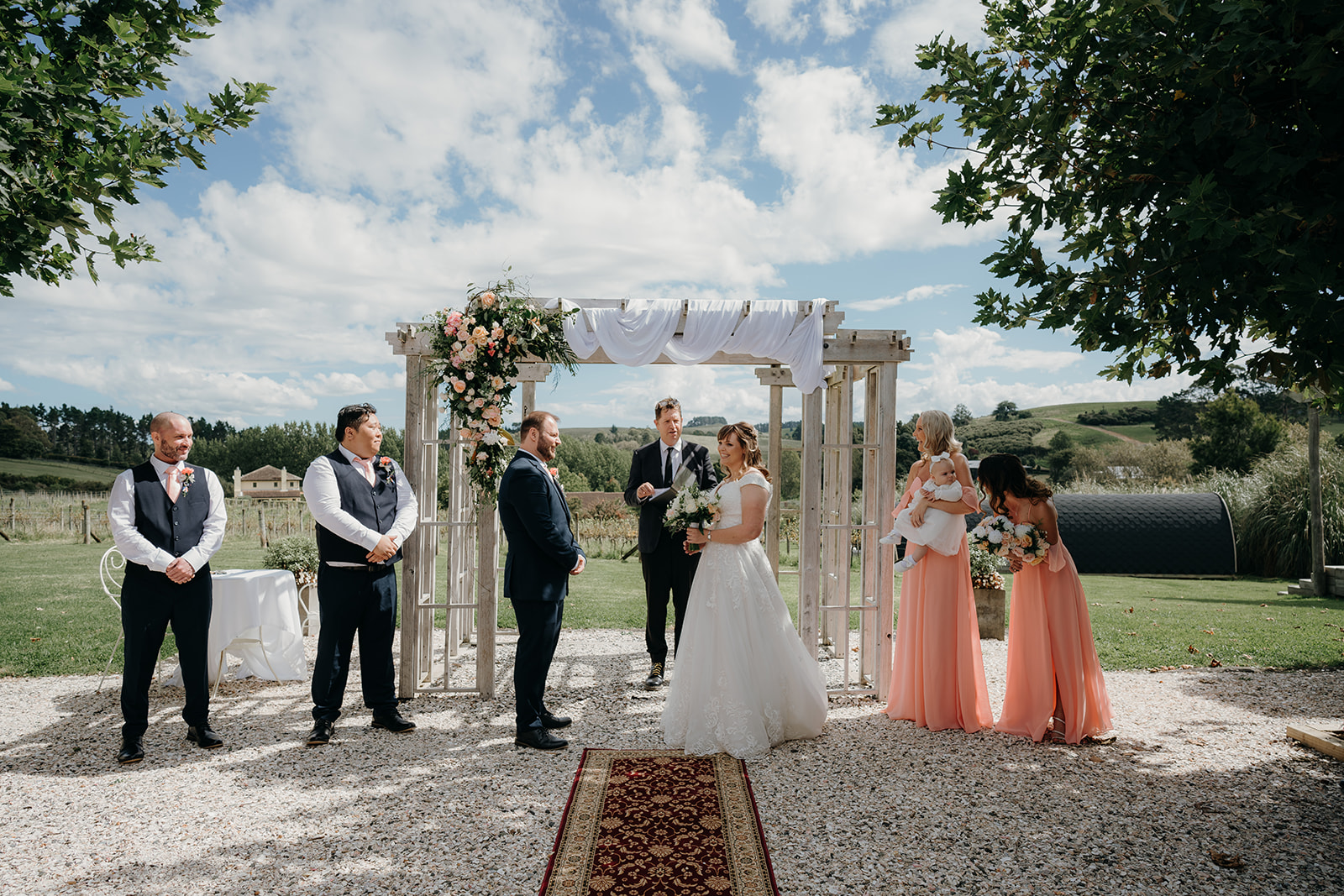 the whole bridal party stand at the alter at turanga creek wedding venue with blue skies above 