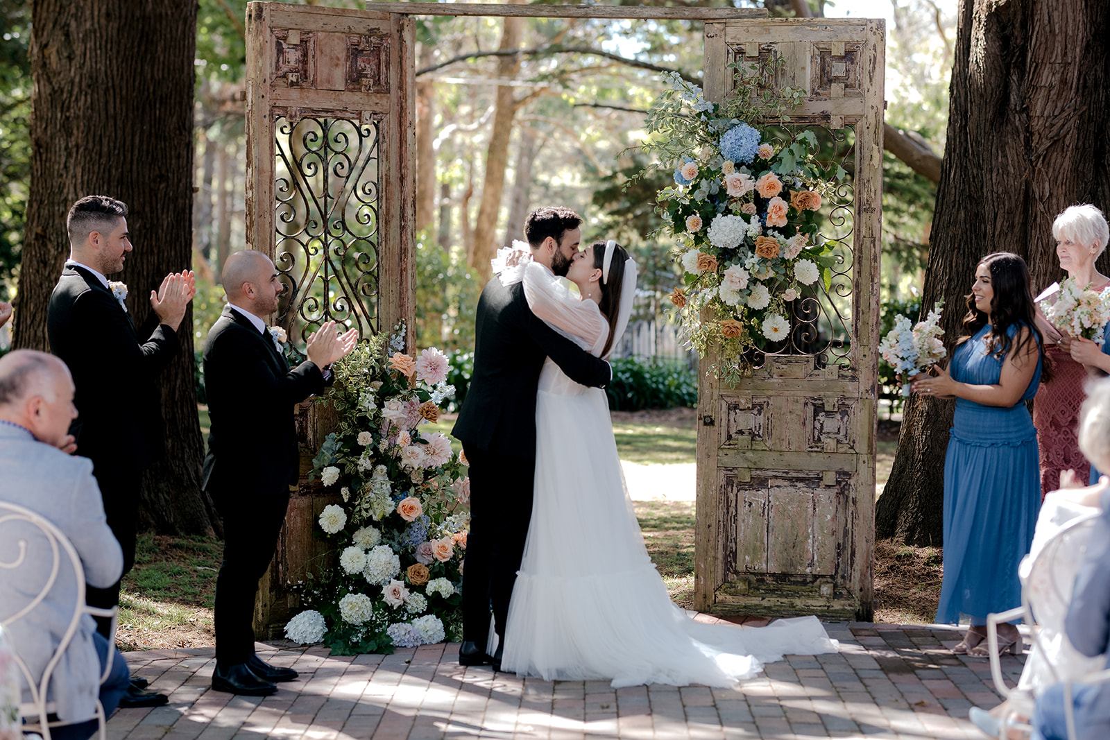 Portrait of bride & groom exchanging their first kiss at their elegant country wedding ceremony.