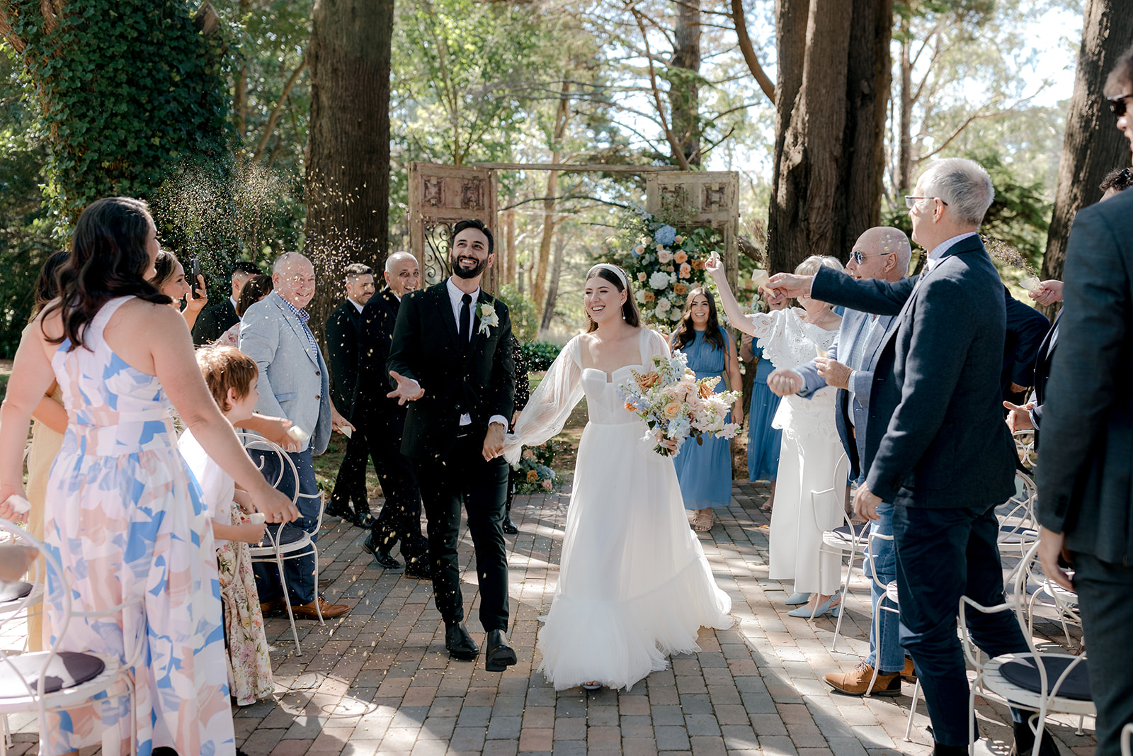 Bride & groom walking up the aisle under a sea of confetti after their elegant country wedding ceremony.