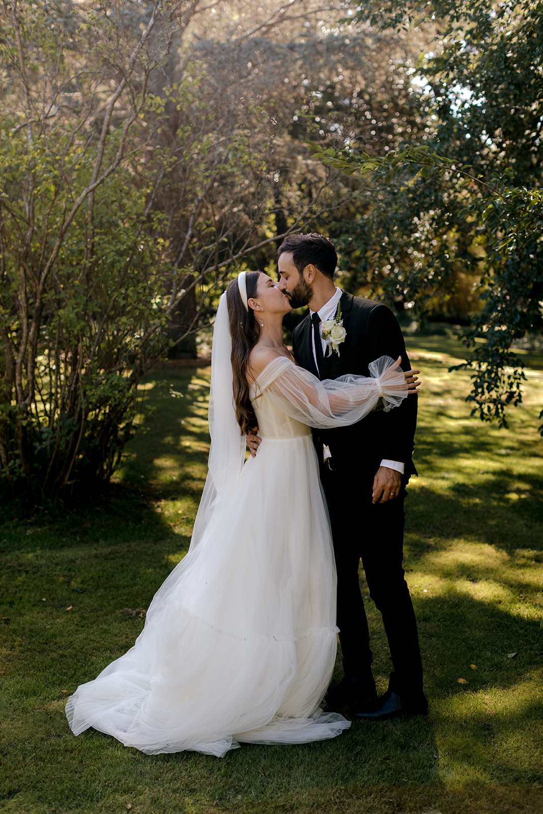 Portrait of bride & groom kissing in an English-inspired garden during their elegant country wedding.
