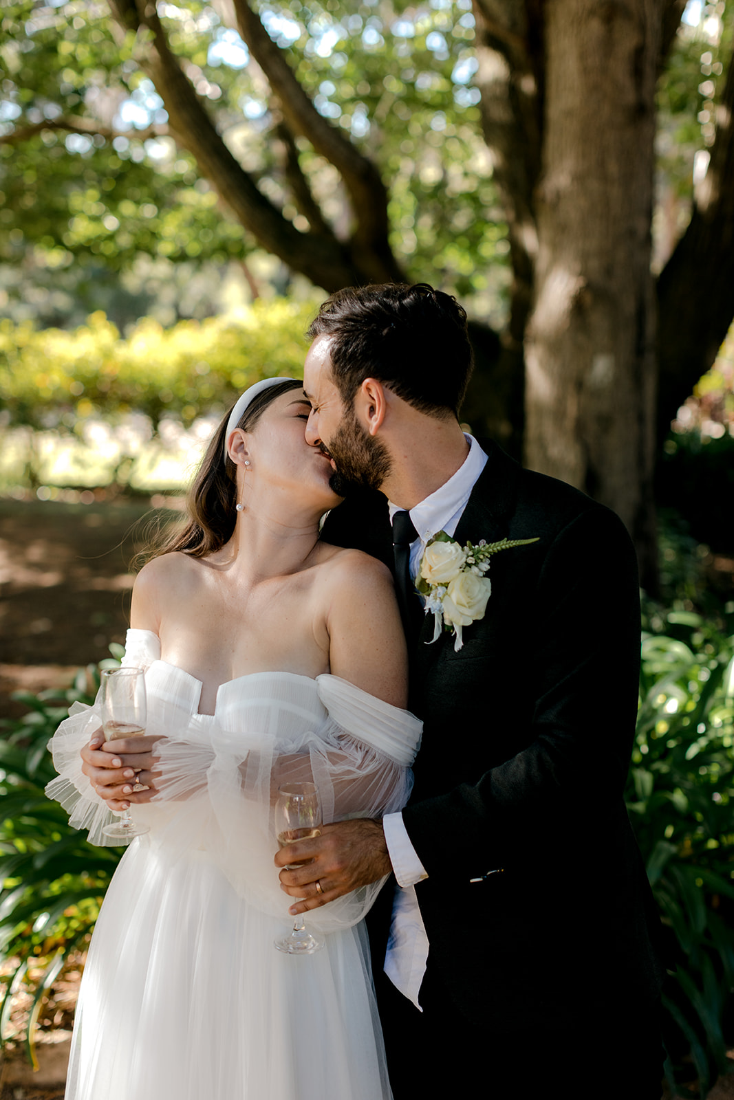 Intimate portrait of bride & groom kissing in an English-inspired garden during their elegant country wedding.