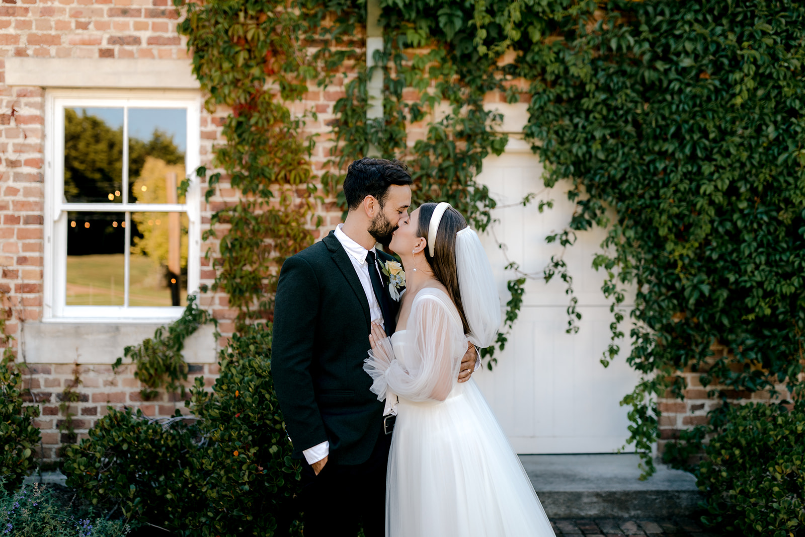 Portrait of bride & groom kissing in front of heritage venue at their elegant country wedding.