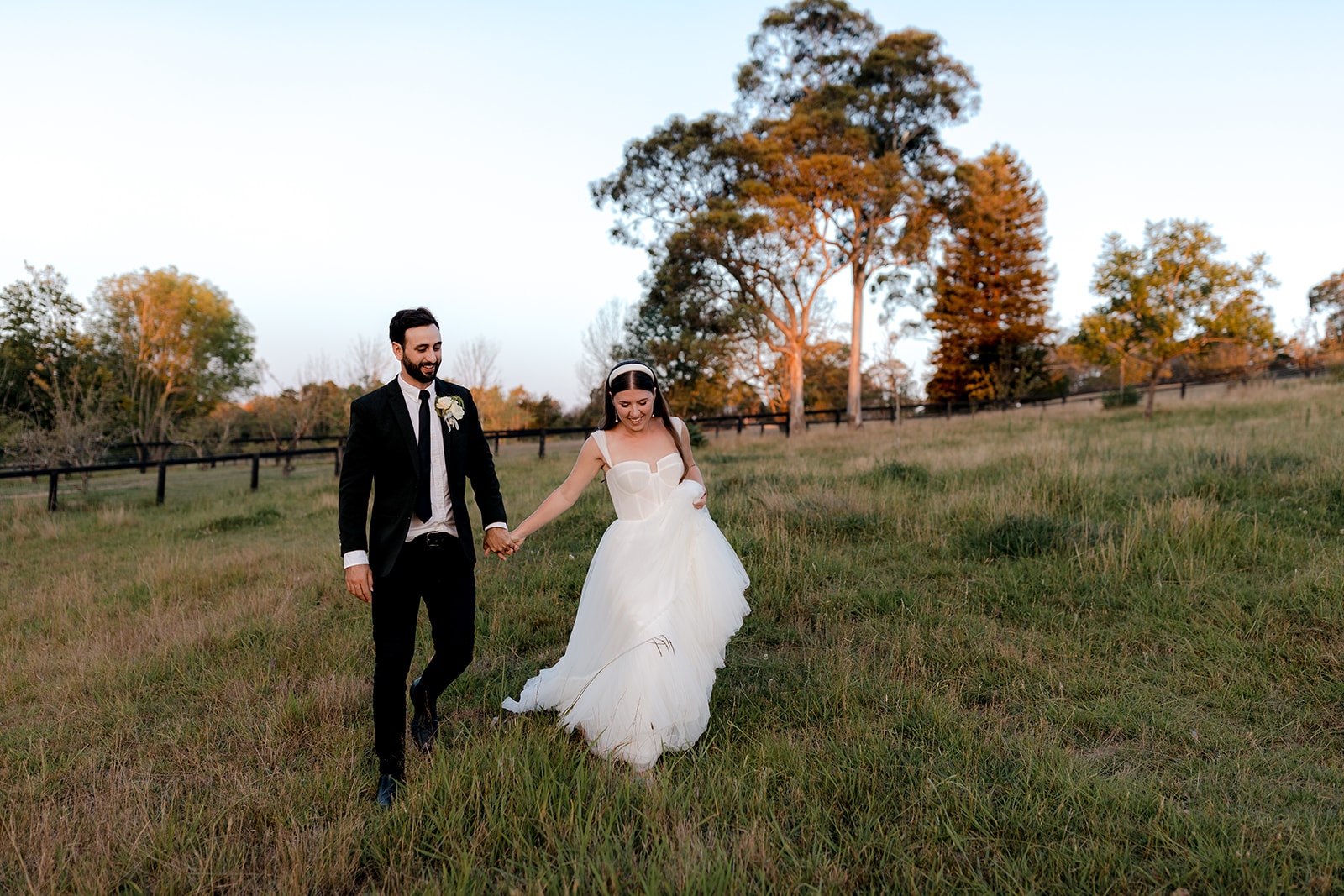 Bride & groom walking hand-in-hand at sunset during their elegant country wedding.