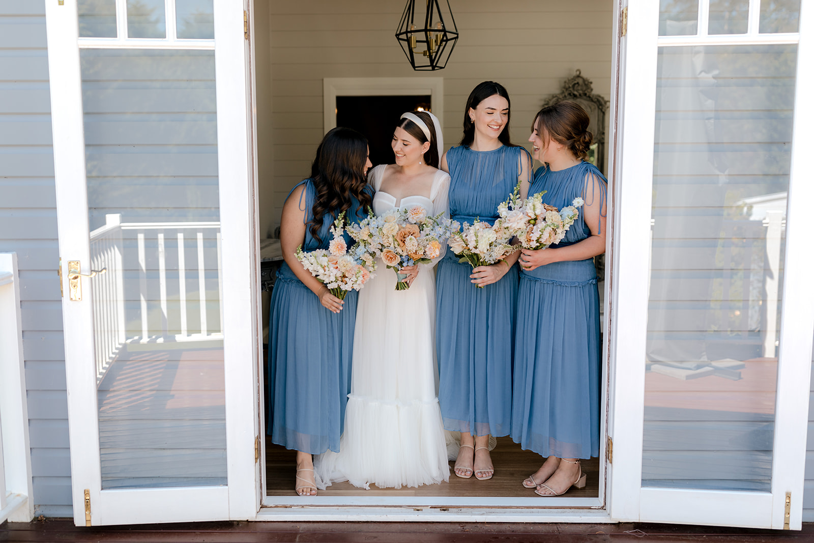 Bride with her bridesmaids holding their bridal bouquets before her elegant country wedding.