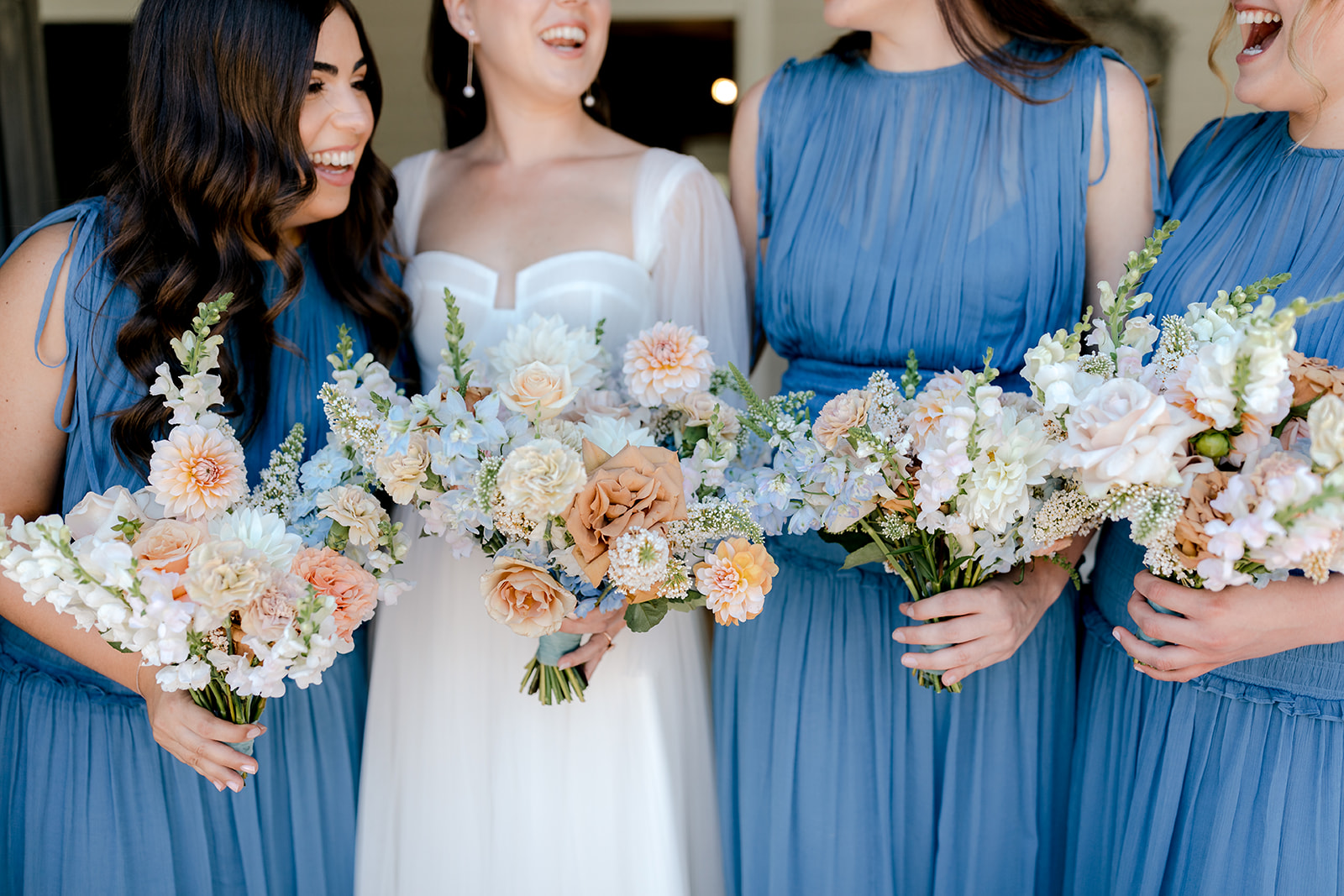 Close-up of bride with her bridesmaids holding their bridal bouquets before her elegant country wedding.