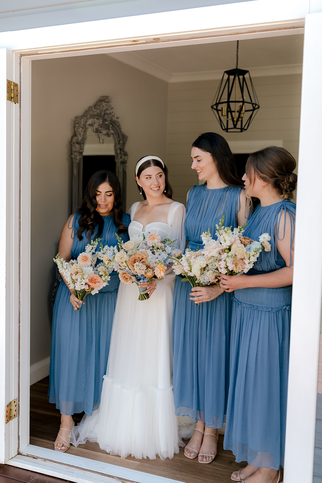 Bride with her bridesmaids holding their bridal bouquets before her elegant country wedding.