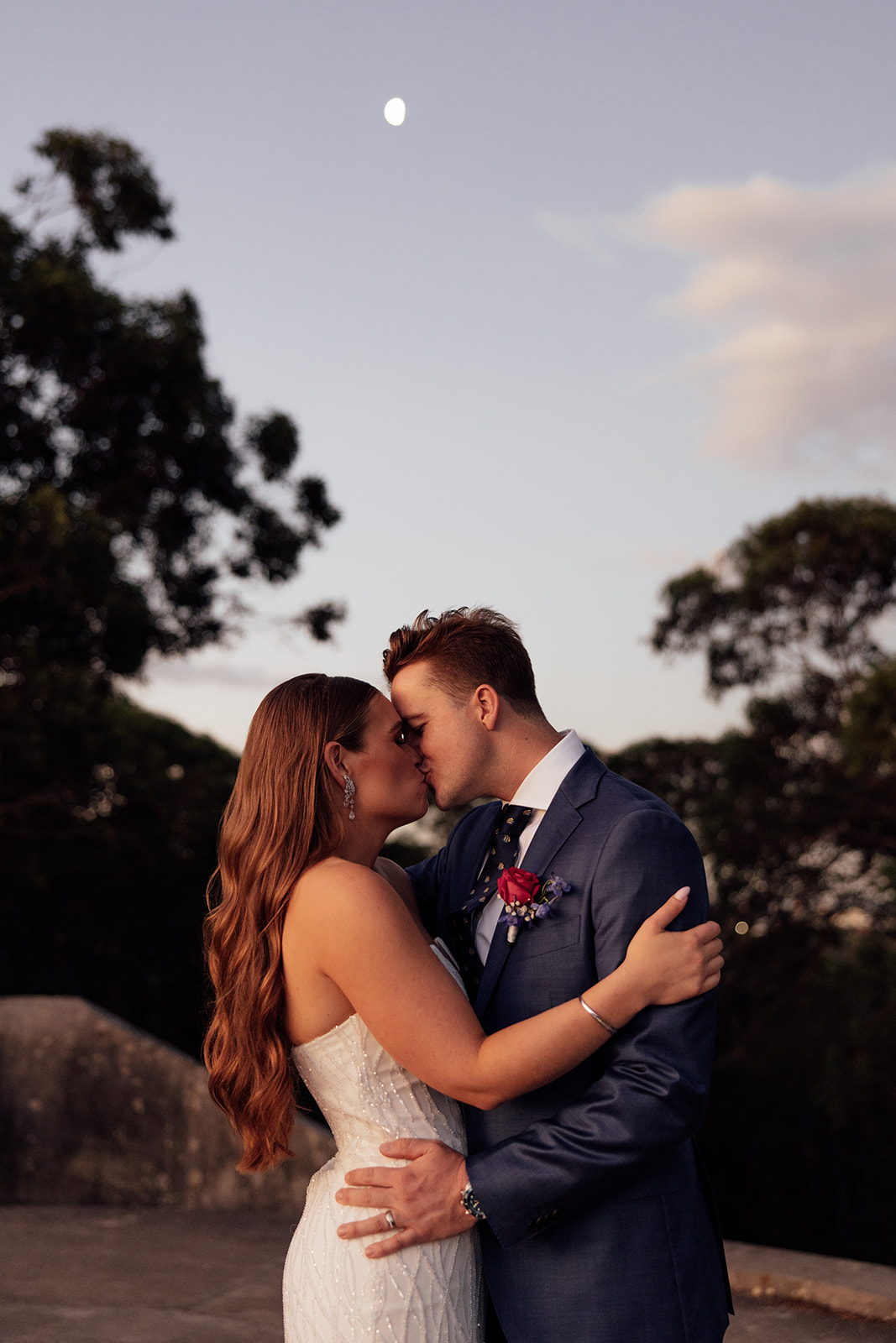 A bride and groom kissing with the moon in the background