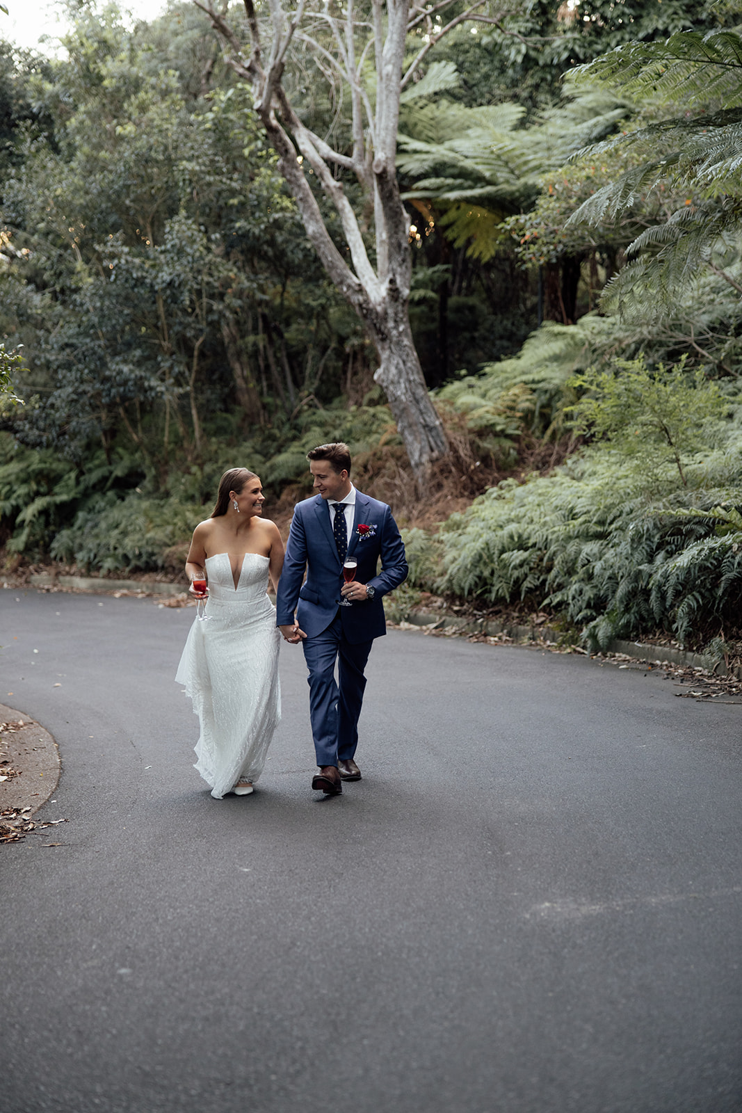 A bride and groom walking up a road with trees