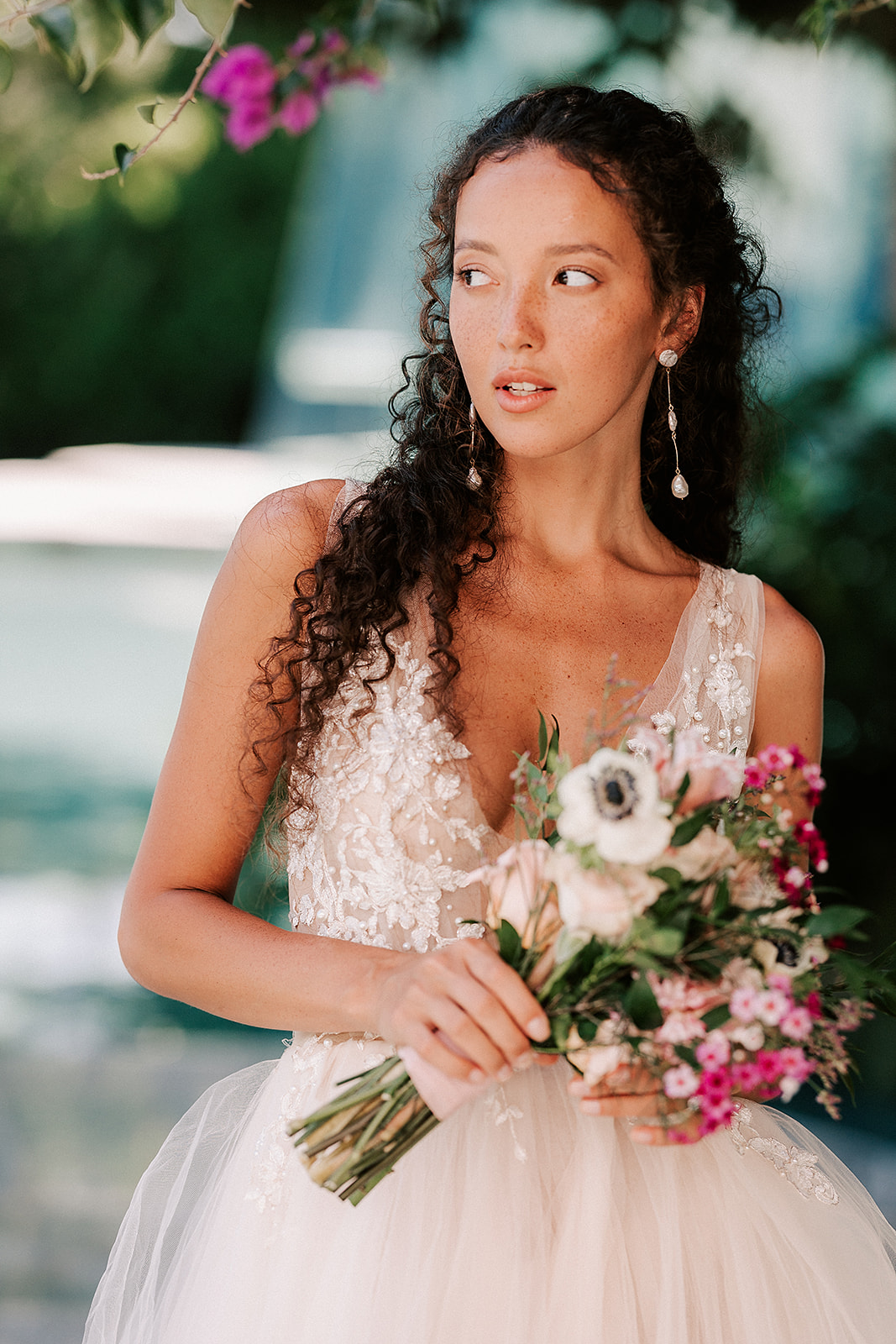 bride is holding her bouquet and looking into the distance with the sparkling blue water behind her