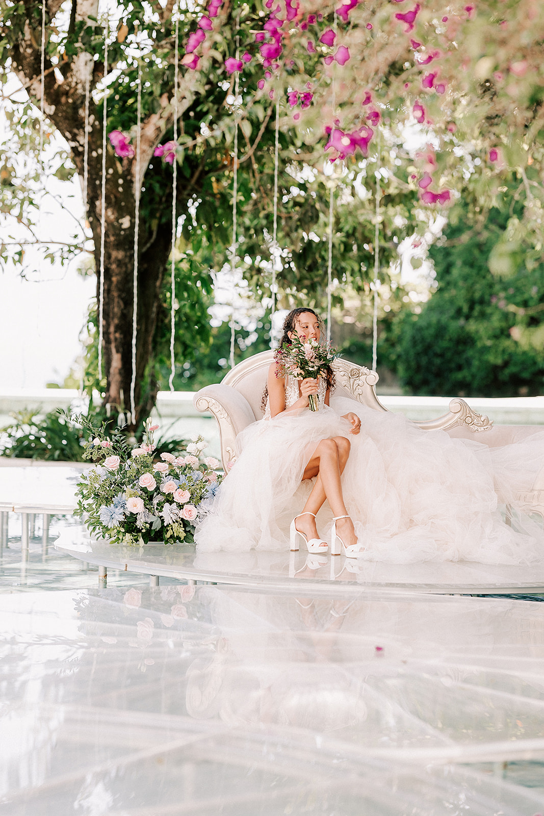 bride sitting on a couch surrounded by florals and underneath a pink tree