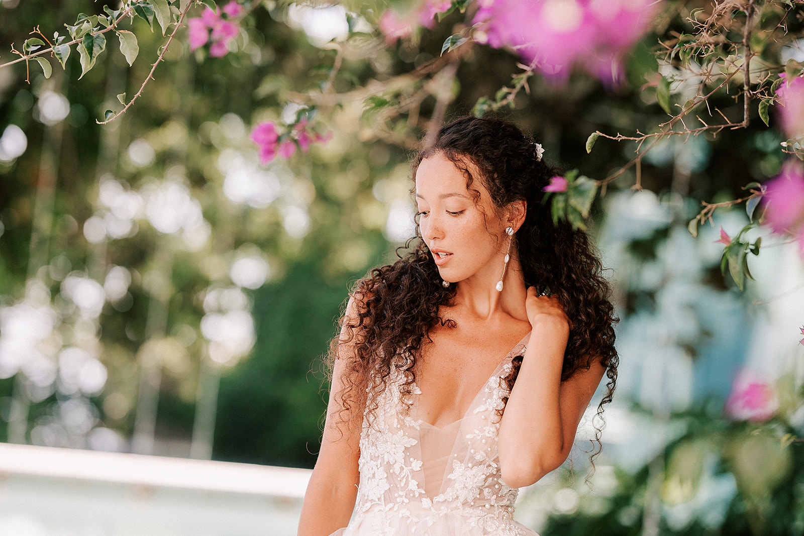 bride touching long curly hair, standing under a tree with pink flowers