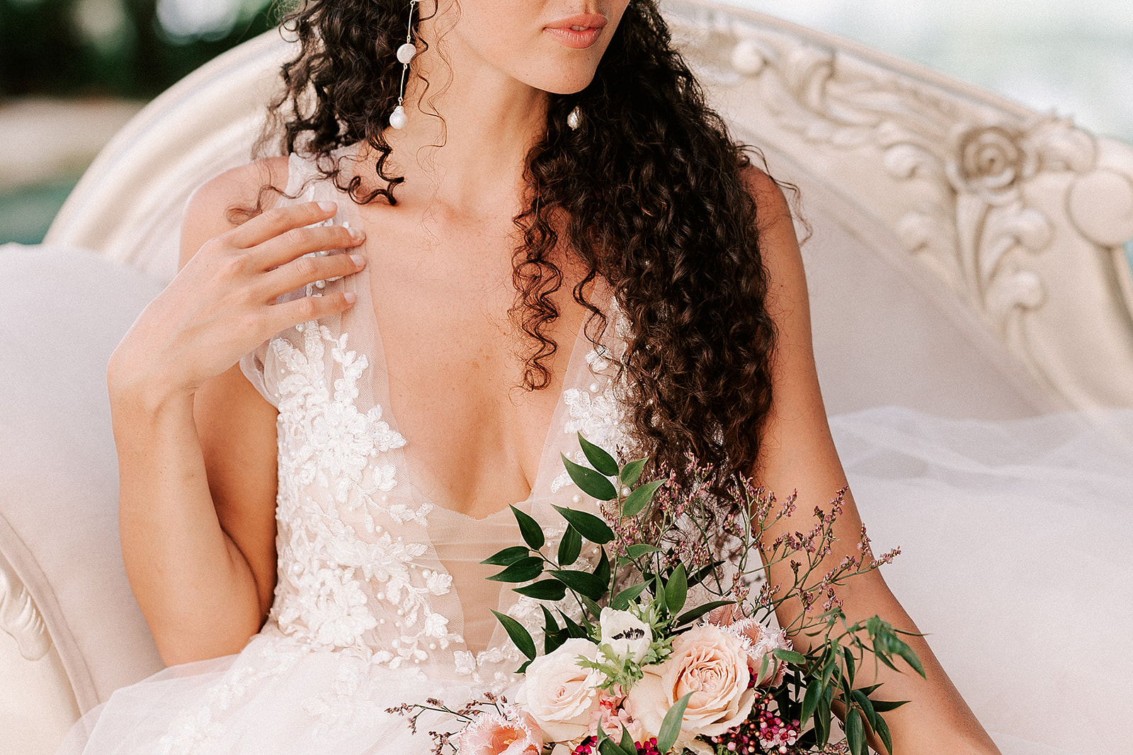 close up of bride stroking the strap of her lace dress, with her bouquet on her lap