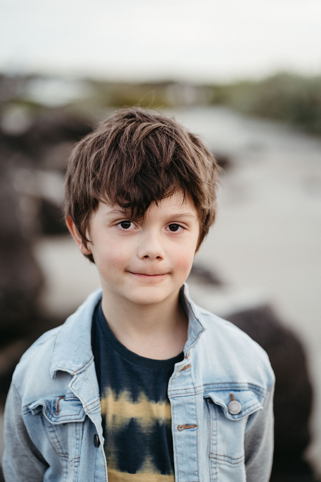 a portrait of a young boy at the beach in a denim jacket
