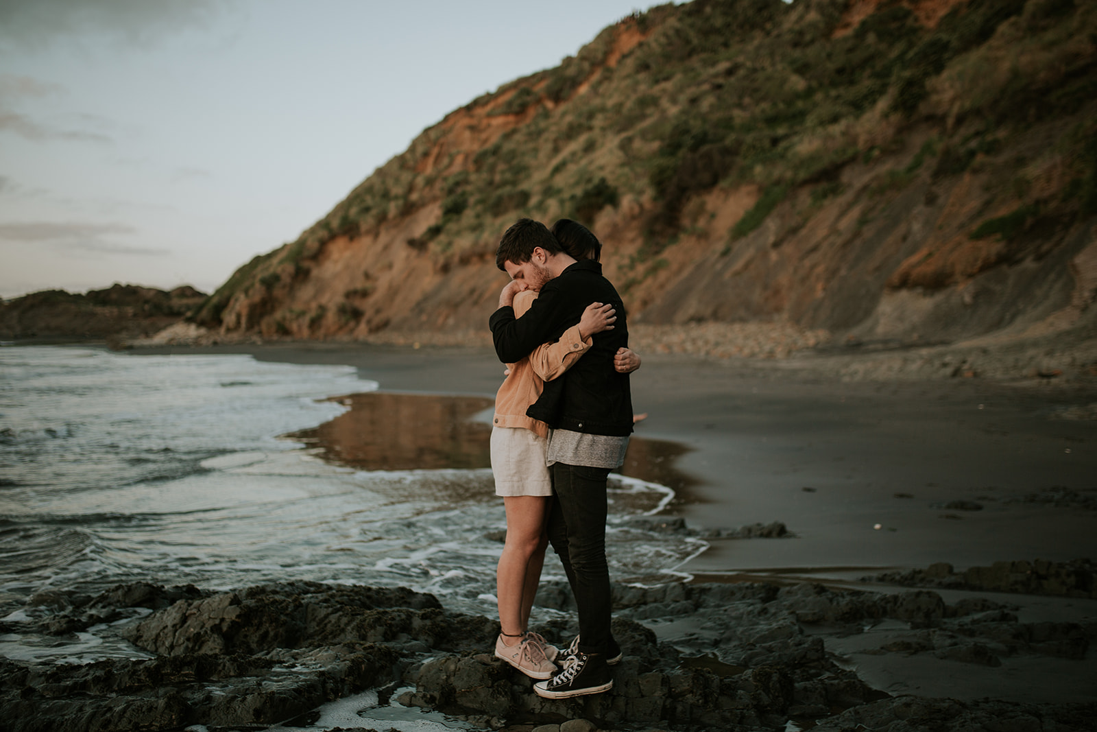 Couple holding each-other in a close embrace while standing on the rocky shore.