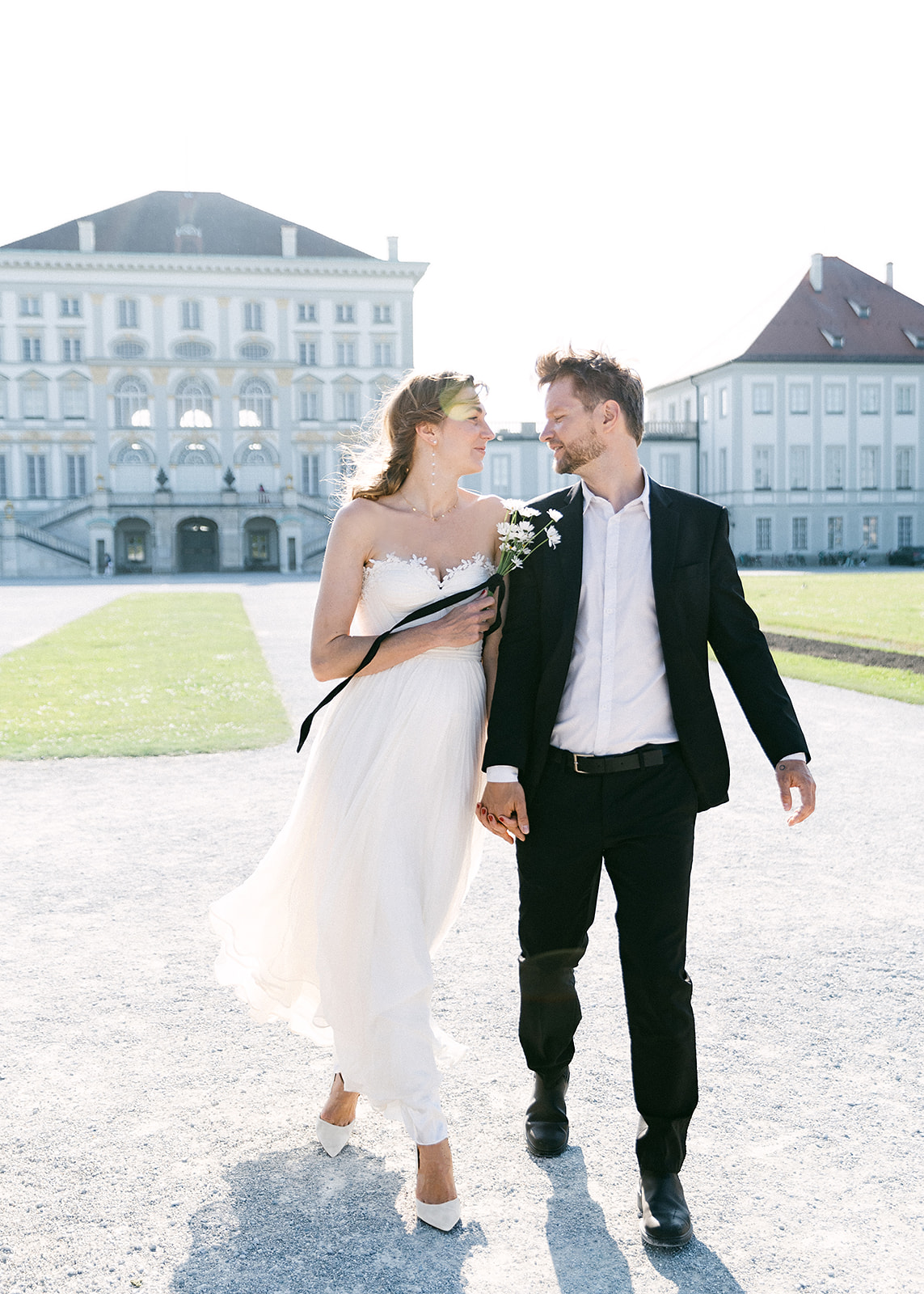 Bride and groom walk in front of Schloss Nypmhenburg for their wedding portraits