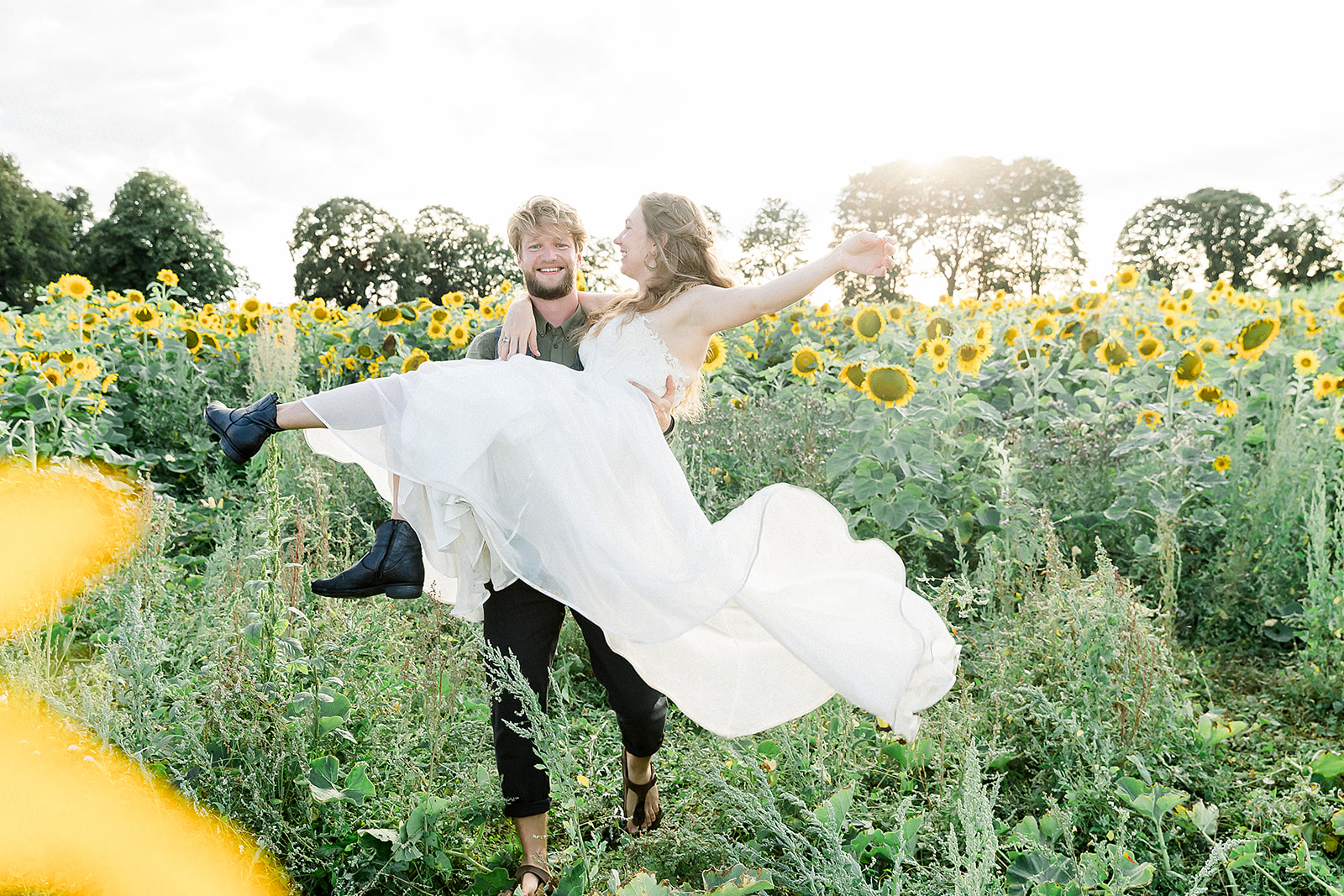Groom carries his bride through a sunflower field in Munich