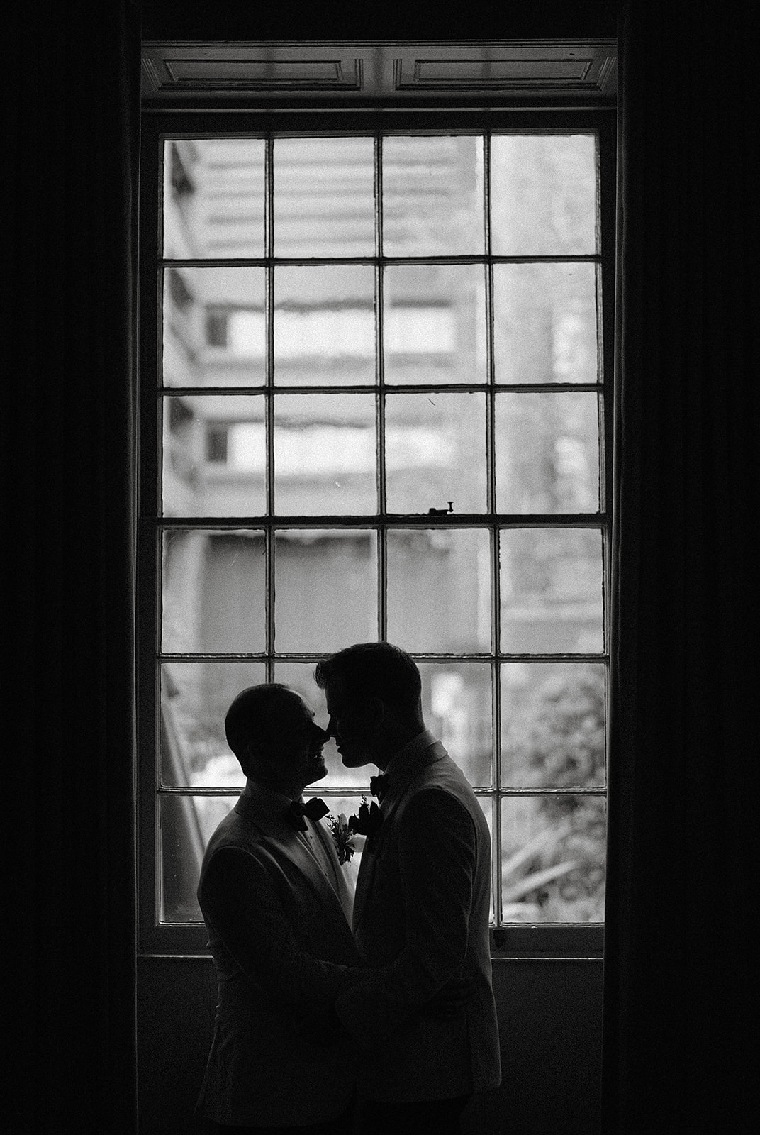A silhouette of two grooms in front of an old fashioned window frame at their same sex Sydney Mint wedding.