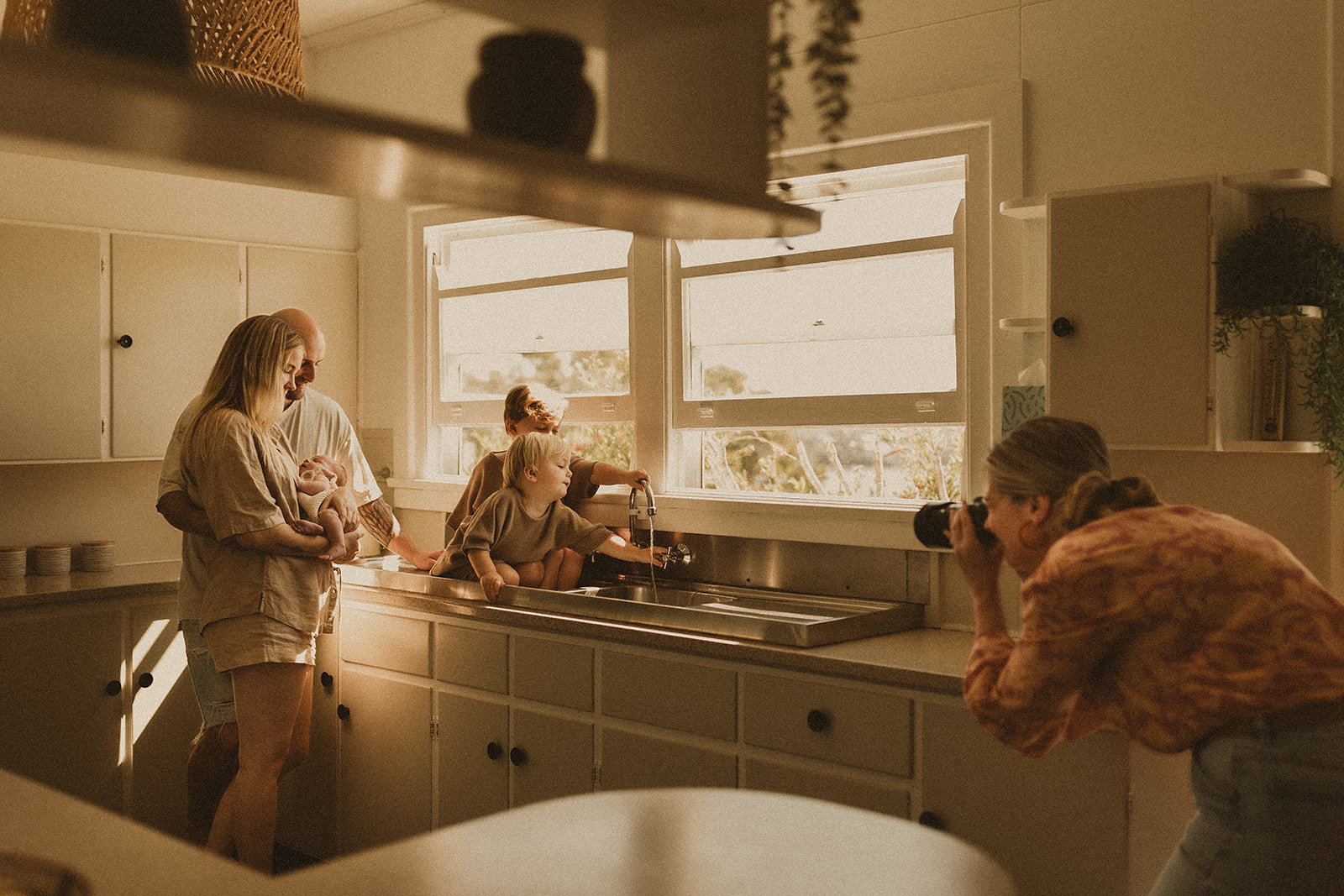 Newborn lifestyle photographer, capturing a family with a newborn and two small children playing at the kitchen sink