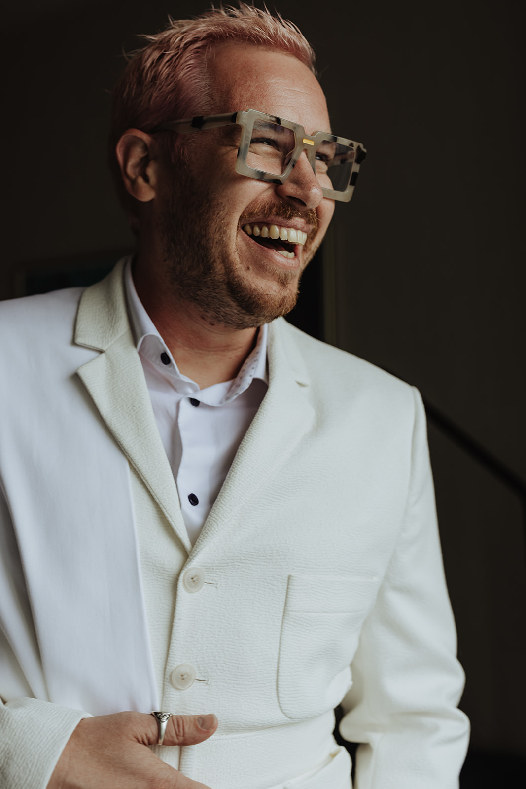 groom wearing white suit and fashion glasses laughing on wedding day