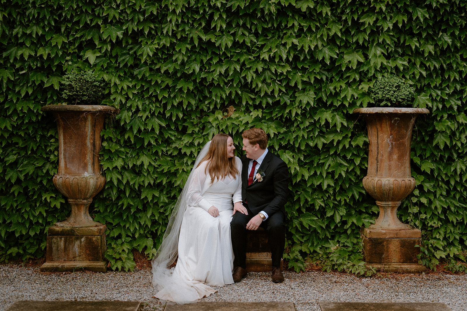 A bride and groom sitting in front of a manicured wall at their Milton Park Country House wedding.