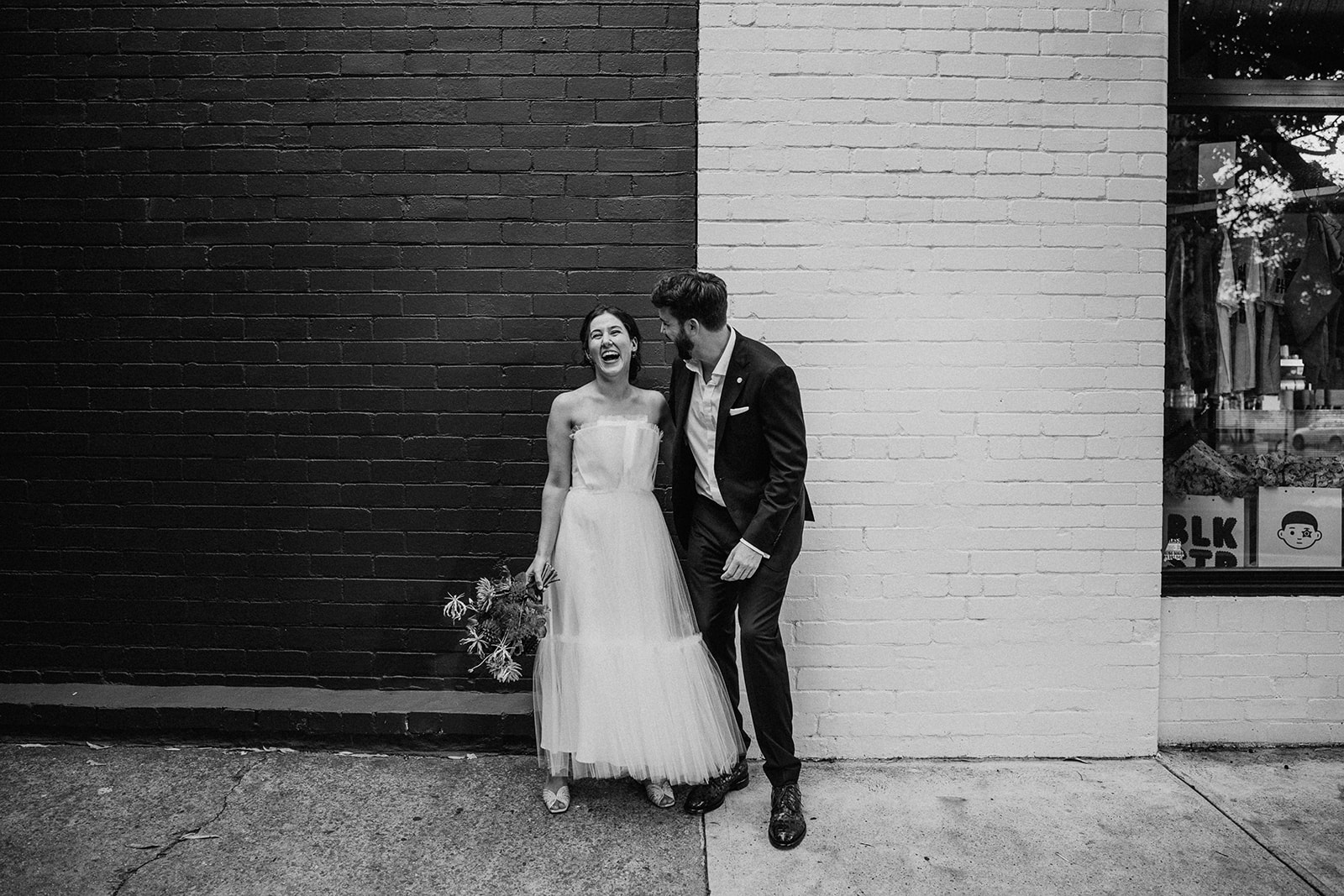 Scott Surplice portrait of bride and groom on black and white wall as couple laugh